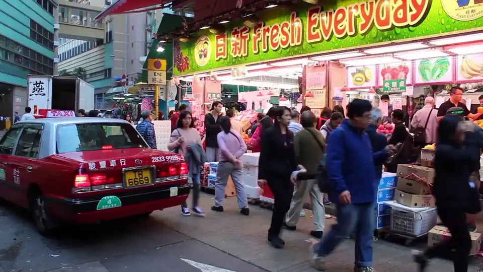 A Hong Kong street market with red taxis and crowds