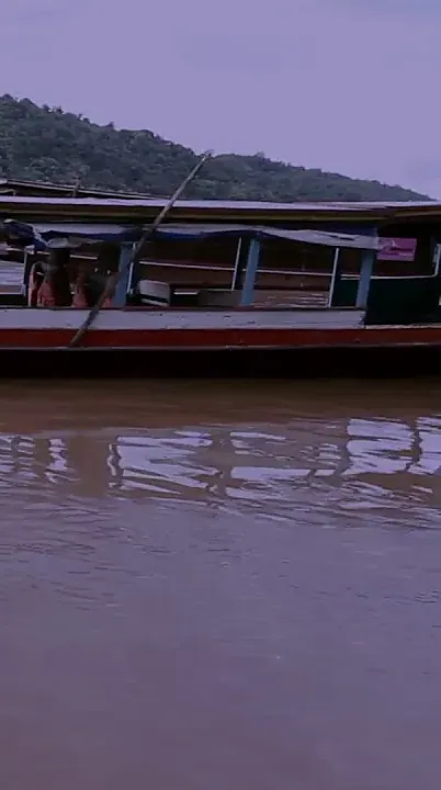 A long wooden boat moored on the brown, swollen Mekong