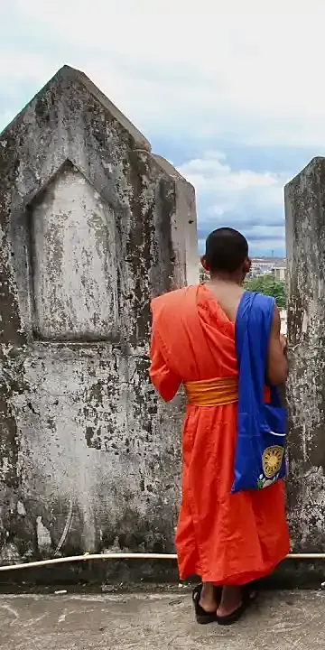 A young monk in an orange robe looking out over an old temple wall
