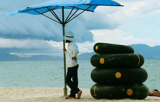 A beach vendor under a blue umbrella next to stacked inflatable rings